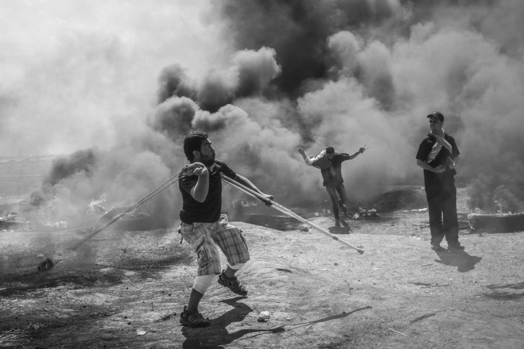 SHEJAIYA, GAZA: Wael, à gauche, lance des pierres vers les soldats iraéliens malgré ses blessures aux jambes dues à une manifestationn précédente, le 14 mai 2018. Le 30 mars, les Palestiniens de Gaza ont décidé pour lancer le mouvement "Grande marche du retour" qui se déroule sur un sit-in et campe aux frontières jusqu'au 15 mai, date de la Nakba, afin de réclamer leur droit au retour.