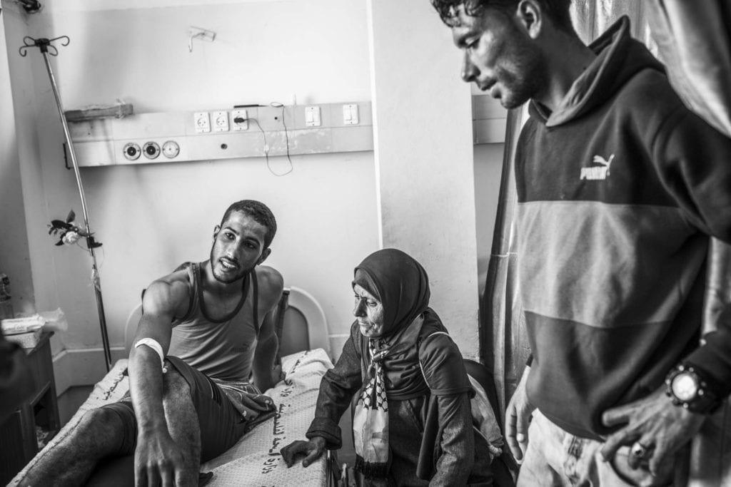 GAZA CITY, GAZA: Oum Wissam, au milieu, rend visite à Mohammed, l'un des Shebab, à l'hôpital Al Shifa. Mohammed a été touché par une balle explosive qui lui a brisé une partie de ses os du pied droit alors qu'il brûlait des pneus près de la clôture entre Israël et Gaza, le 15 mai 2018. Le 30 mars, les Palestiniens de Gaza ont décidé pour lancer le mouvement "Grande marche du retour" qui se déroule sur un sit-in et campe aux frontières jusqu'au 15 mai, date de la Nakba, afin de réclamer leur droit au retour.