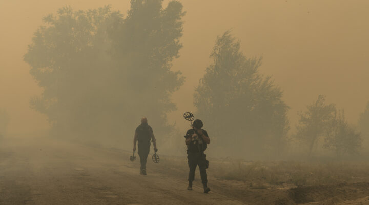 LYMAN, UKRAINE - AUGUST 22, 2024: Deminers carrying metal detectors walk through thick smoke from a wildfire presumably caused by shelling on Thursday, August 22, 2024 in Lyman, Ukraine. Large portions of eastern Ukraine's forests have been severely damaged by war-related wildfires, and fighting them is complicated by the presence of enemy forces, landmines, and unexploded ordnance. © Brendan Hoffman